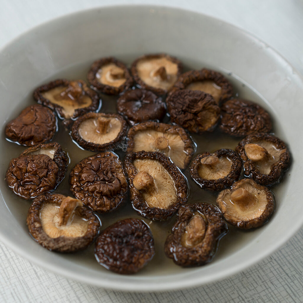 Dried shiitake mushrooms soaking and rehydrating in a bowl of ho